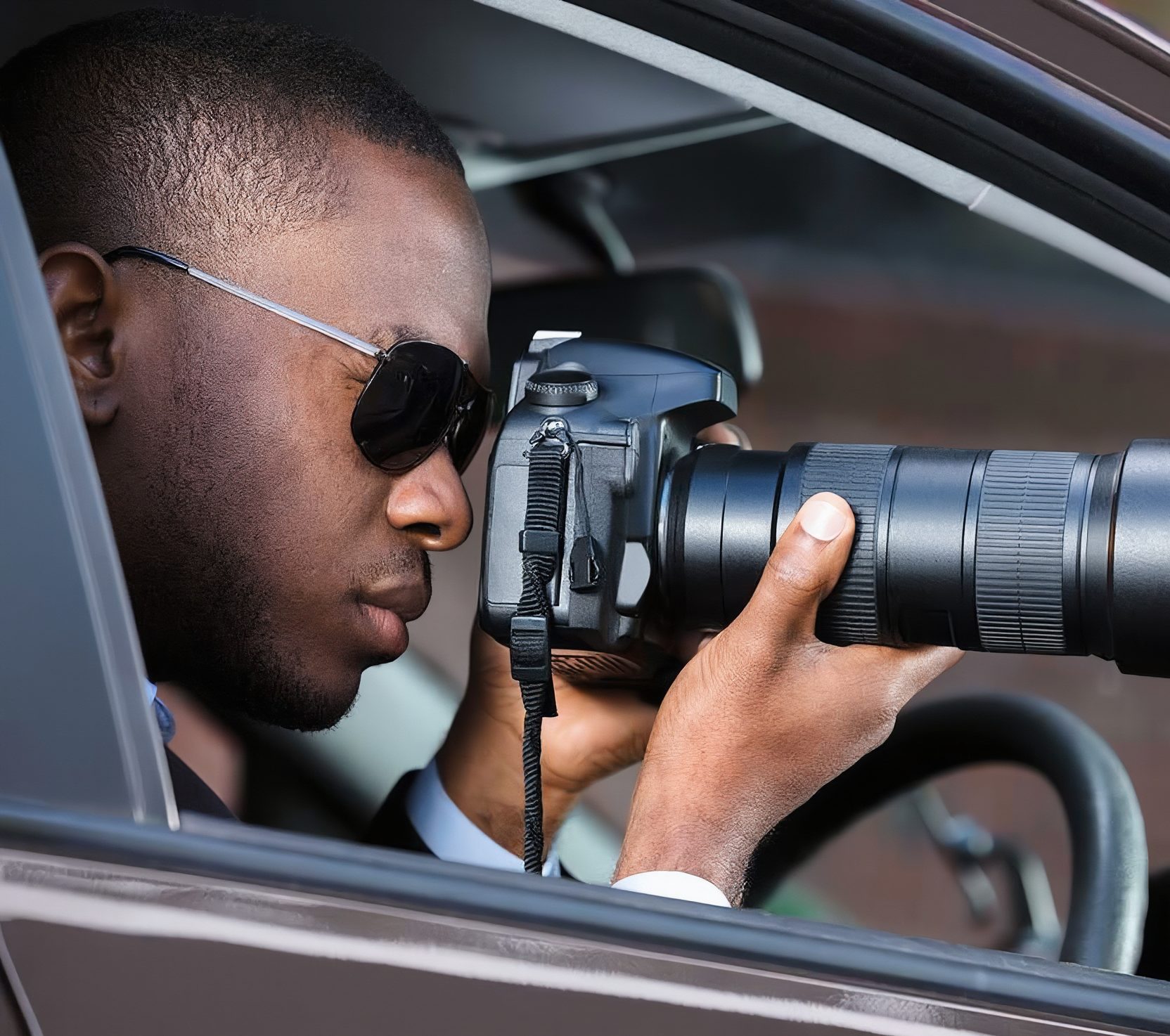 Investigator in sunglasses photographing with a telephoto camera from inside a car